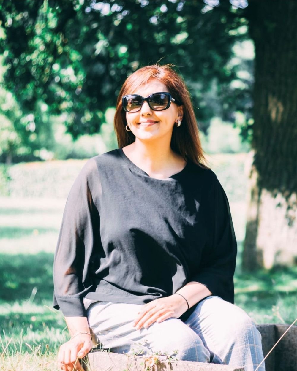 Humma sitting outdoors beneath a tree on a sunny day